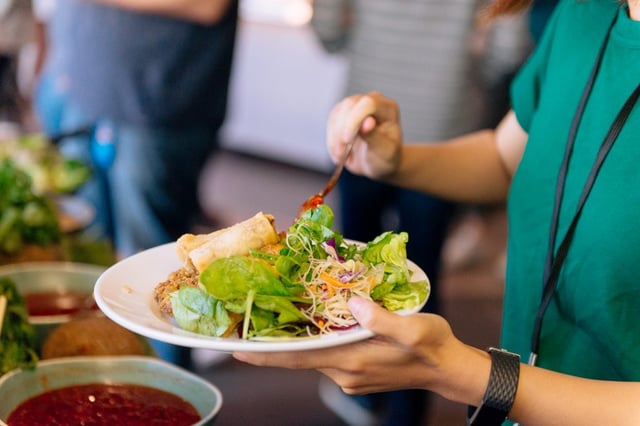 An employee serving themselves a plate of salad from a corporate caterer's buffet offering