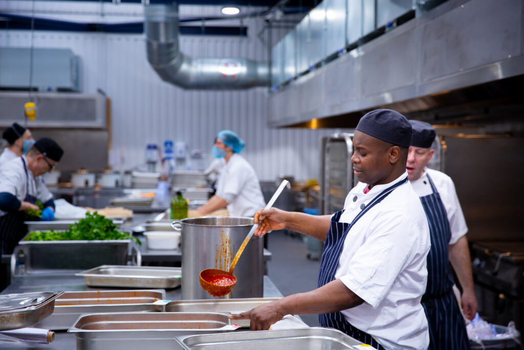A chef with a soup ladle in a busy kitchen 