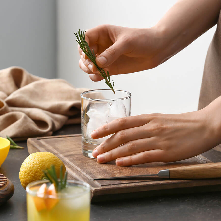 A rosemary sprig being placed in a glass of ice