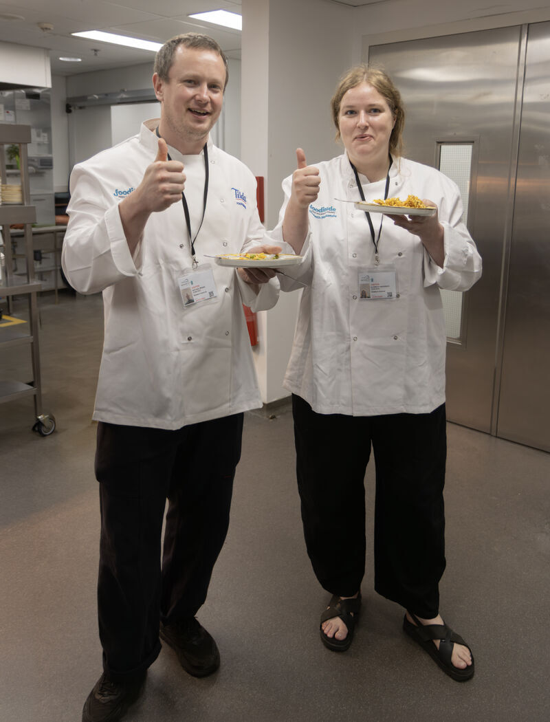 Fooditude chefs giving a thumbs up with their dishes in the kitchen